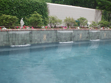 Waterfalls pouring out of raised wall on pool.