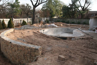 A pool with the decking removed and a wall around it.