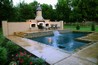 Pool with a raised tiled wall with a waterfall and a fireplace on a raised deck.