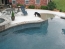A black dog drinking water out of a pool at the beach entry.
